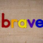 Colorful felt letters forming the word 'brave' on a burlap background.